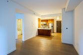 Located at 225 S Grand Ave in downtown Los Angeles, this modern residence offers a well-designed layout with refined finishes throughout. The open-concept kitchen is a standout feature, outfitted with rich walnut cabinetry, crisp white countertops, a tile backsplash, and stainless steel appliances including a range, microwave, and refrigerator. A peninsula with a single-basin sink and pendant lighting creates a natural gathering point and adds visual warmth to the space. The living area flows seamlessly from the kitchen, with light wood flooring, clean white walls, and louvered utility closet doors that maintain the home's clean aesthetic. Bedrooms feature wood flooring in varying tones and large windows that frame views of the surrounding downtown Los Angeles skyline and palm-lined streetscapes, allowing natural light to fill each room. One bedroom includes a built-in closet with simple, modern hardware. The bathroom is finished with full marble-tiled walls, a soaking tub with glass enclosure, a walnut vanity with a marble countertop, and a large mirror with overhead lighting. Throughout, the design balances warm wood tones with neutral palettes, delivering a contemporary and functional urban living environment.