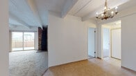 This single-floor residence showcases a distinctive architectural character defined by exposed ceiling beams and a textured ceiling throughout. The spacious living area is anchored by a striking brick accent column and is finished with neutral wall-to-wall carpeting, creating a warm and open atmosphere. Large sliding glass doors lead to a private balcony, offering expansive urban views and abundant natural light. An additional room with a dedicated balcony access door further enhances the connection to the outdoors.

The galley-style kitchen is outfitted with rich wood cabinetry, dark granite countertops, a stainless steel refrigerator, and a pass-through bar that opens toward the dining area. Light tile flooring runs through the kitchen and entryway, providing a clean contrast to the carpeted living and bedroom spaces. A decorative chandelier adds a classic touch to the dining area.

The bedrooms are generously proportioned, each featuring soft carpeting, beamed ceilings, and ample natural light. The bathroom includes tile flooring, wood cabinetry with granite countertops, a mirrored sliding door, and a separate water closet. Overall, the space offers a functional layout with a mix of classic and updated finishes throughout.