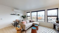 Located on SE Belmont Street in Portland's vibrant Capitol Hill neighborhood, this modern residence offers a thoughtfully designed single-floor layout with clean lines and a bright, contemporary aesthetic throughout. The open-concept living and dining area is anchored by large black-framed windows that frame sweeping views of the Portland skyline, flooding the space with natural light and creating a seamless connection to the urban landscape. Light hardwood flooring runs throughout, complementing the crisp white walls and lending warmth to the interior. A ductless mini-split system provides efficient climate control in the main living area. The kitchen is outfitted with dark cabinetry, light quartz countertops, a white subway tile backsplash, and stainless steel appliances including a gas range and built-in microwave. Both bedrooms are generously sized, each featuring black-framed windows with city views and ample natural light. The two bathrooms are finished with dark vanity cabinetry, light countertops, and tub/shower combinations. A conveniently placed hallway closet houses a full-size stacked washer and dryer. The entry corridor offers practical wall hooks for storage, with the bright living spaces visible beyond — making this residence a well-appointed urban retreat in the heart of Portland.