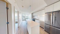 Located in Calgary, AB, this thoughtfully designed one-bedroom, one-bathroom unit offers a modern and efficient layout with clean finishes throughout. The open-concept living and kitchen area anchors the space, featuring warm wood-look laminate flooring and crisp white walls that create a bright, airy atmosphere. A sleek kitchen showcases flat-panel white cabinetry extending to the ceiling, stainless steel appliances including a gas range and French door refrigerator, and a white quartz waterfall island that doubles as a dining surface, illuminated by a contemporary linear pendant light. A hallway with a sliding barn door connects the living area to the bedroom and bathroom, adding a stylish architectural touch. The bedroom is a well-proportioned retreat with access to two separate closets, keeping the space clean and organized. Floor-to-ceiling windows frame sweeping views of the Calgary skyline, flooding the unit with natural light. The bathroom is finished with large-format white tile surrounding a full soaker tub with an adjustable showerhead. Throughout the unit, the consistent use of white tones, modern hardware, and natural-toned flooring delivers a cohesive, contemporary aesthetic suited for urban living.