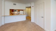 This single-floor, 1-bedroom, 1-bathroom unit in Concord offers a practical and comfortable layout designed for easy everyday living. The open-concept living and kitchen area serves as the heart of the home, where a curved breakfast bar counter seamlessly connects the kitchen to the living space. The kitchen is equipped with wood-toned cabinetry, a white appliance suite including a refrigerator, electric range, and over-the-range microwave, and a sink positioned along the bar for added convenience. Crown molding accents the living area, which features soft carpeting and a ceiling fan with light fixture, while windows fitted with blinds allow for natural light and privacy. The bedroom is a calm, carpeted retreat with a window that brings in ample natural light, clean white walls, and generous proportions suitable for various furniture arrangements. The full bathroom is finished with light tile flooring, warm oak cabinetry beneath a single-basin vanity with a white countertop, a large mirror with overhead lighting, a wall-mounted storage cabinet, and a toilet. The unit's neutral color palette and clean finishes create a bright, move-in-ready atmosphere throughout.