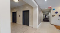 This single-floor amenity space is thoughtfully designed to serve a variety of social, recreational, and professional needs. The entry lobby sets an impressive tone with large globe pendant lights, colorful wall-mounted art installations, glass railings, and warm cove lighting that creates an inviting first impression.

The co-working area features long white tables, modern black chairs, and a counter-height bar along one wall, all set against yellow-green accent walls beneath an exposed black ceiling with track lighting. A separate lounge nook provides a more intimate setting with rounded upholstered ottomans, a textured side table, wall sconces, and a wall-mounted television.

The game room is styled with dark wood wainscoting, hardwood-style flooring, vintage-inspired framed artwork, a foosball table, billiards, an arcade cabinet, and leather seating arranged around mounted screens. A sport court area features bold royal blue padded walls, light wood flooring, and high ceilings for active use.

Additional private pods with patterned wallcovering and small tables offer quiet work options, while a separate lounge with stone-textured walls and a media console provides a calm, contemporary retreat.