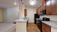 Located at 100 Ward Strasse in the scenic mountain town of Leavenworth, Washington, this single-floor unit offers a thoughtfully designed layout with a warm, neutral color palette throughout. The open-concept kitchen is a standout feature, showcasing rich medium-tone wood cabinetry, granite-style countertops, and a peninsula with a double sink and decorative amber pendant lighting. Black appliances, including a refrigerator, range, and built-in microwave, complement the hardwood-style flooring that runs through the kitchen area. The living space transitions to plush wall-to-wall carpet and features vaulted ceilings that enhance the sense of openness and airiness. A glass-panel entry door allows natural light to filter into the main living area. The bedrooms are carpeted and well-lit, with windows offering serene, wooded views of the surrounding Pacific Northwest landscape. The bathroom is finished with matching granite-style countertops, warm wood cabinetry, oil-rubbed bronze hardware, a large vanity mirror, and hardwood-style flooring. Each room reflects a consistent and cohesive design aesthetic, making this a comfortable and visually appealing residence in the heart of the Cascades.