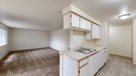 This single-floor residence is designed with a practical, open layout that connects the kitchen and living area seamlessly. The kitchen is well-equipped, featuring white cabinetry with light wood trim accents, ample upper and lower cabinet storage, light-colored laminate countertops, a stainless steel double-basin sink, a white electric range, a dishwasher, and a refrigerator. Light wood-look flooring runs throughout the kitchen, providing a clean, easy-to-maintain surface. A peninsula counter extends into the space, offering additional workspace and a natural transition into the carpeted living area.

The living space is generously proportioned, with neutral-toned carpet and smooth walls finished in a soft, warm white. The textured ceiling adds subtle visual interest throughout. Bedroom areas are carpeted as well, offering a comfortable and quiet atmosphere, with closet access visible in at least one room.

The bathrooms include a full bath with a soaking tub and handheld showerhead combo, and a second bath featuring a walk-in shower with sliding glass doors, a wide vanity with under-sink storage, a large mirror, and tile flooring. A dedicated in-unit laundry area accommodates a full-sized washer and dryer with overhead shelving for additional storage.