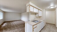 This single-floor residence is designed with a practical, open layout that connects the kitchen and living area seamlessly. The kitchen is well-equipped, featuring white cabinetry with light wood trim accents, ample upper and lower cabinet storage, light-colored laminate countertops, a stainless steel double-basin sink, a white electric range, a dishwasher, and a refrigerator. Light wood-look flooring runs throughout the kitchen, providing a clean, easy-to-maintain surface. A peninsula counter extends into the space, offering additional workspace and a natural transition into the carpeted living area.

The living space is generously proportioned, with neutral-toned carpet and smooth walls finished in a soft, warm white. The textured ceiling adds subtle visual interest throughout. Bedroom areas are carpeted as well, offering a comfortable and quiet atmosphere, with closet access visible in at least one room.

The bathrooms include a full bath with a soaking tub and handheld showerhead combo, and a second bath featuring a walk-in shower with sliding glass doors, a wide vanity with under-sink storage, a large mirror, and tile flooring. A dedicated in-unit laundry area accommodates a full-sized washer and dryer with overhead shelving for additional storage.