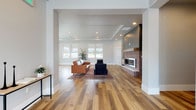 This single-floor space is designed with a modern aesthetic, showcasing an open-concept layout that seamlessly connects the living area and kitchen. Wide-plank hardwood flooring in warm natural tones runs throughout, providing a cohesive and inviting foundation.

The living area is a standout feature, anchored by a floor-to-ceiling fireplace that combines exposed brick with gray shiplap paneling, creating a striking focal point. A tray ceiling with recessed lighting adds architectural depth overhead. Built-in shelving with gray cabinetry flanks the fireplace, offering both display and storage functionality. Multiple windows fitted with roller shades allow ample natural light to fill the space while maintaining privacy.

The kitchen is equally well-appointed, featuring gray shaker-style cabinetry that extends to the ceiling, with glass-front upper cabinets adding visual interest. White quartz countertops contrast cleanly against the cabinetry, and a white subway tile backsplash reinforces the modern palette. A central island provides additional workspace and storage. Stainless steel appliances, including a refrigerator and built-in microwave, complete the kitchen's functional design.

An entry area with a console table provides a transitional space, and the open sightlines throughout ensure the overall ambiance remains bright, spacious, and cohesive.