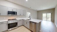 Located at 5790 Stockport St in Riverview, FL, this 2-bedroom, 2-bathroom unit offers a well-designed single-floor layout with a clean, contemporary aesthetic throughout. Light wood-style flooring flows seamlessly across all living areas, complementing the neutral greige wall tones that create a bright, cohesive atmosphere.

The open-concept kitchen and living area serves as the heart of the home. The kitchen is equipped with gray shaker-style cabinetry, white countertops, black hardware accents, and a full suite of stainless steel appliances including a gas range, over-the-range microwave, and refrigerator. The living area benefits from generous natural light and direct access to a private balcony through sliding glass doors, offering pleasant outdoor views.

Both bedrooms are well-proportioned, each featuring natural light from windows with blinds and ceiling fans. The primary bedroom offers comfortable dimensions with its own dedicated bathroom. The primary bath includes a wide vanity with gray cabinetry, white countertop, black fixtures, and a large mirror. The second bathroom features a full tub-shower combination with black hardware accents. A hallway connects the private areas of the unit, and the overall design reflects a modern, move-in-ready finish throughout.