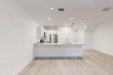 Located at 2737 NW 13th St in Pompano Beach, Florida, this two-story home offers four bedrooms and three bathrooms across two thoughtfully designed floors. The main level features an open-concept living and kitchen area finished in a crisp, all-white palette with light wood-style flooring that flows throughout the space. The kitchen is equipped with stainless steel appliances, including a refrigerator, range, and microwave, complemented by sleek white cabinetry and a generous peninsula countertop with an integrated sink — ideal for both meal prep and casual dining. Recessed lighting illuminates the space evenly, enhancing the bright, airy atmosphere. A light-filled hallway on the main level leads to the staircase, which features wood-toned steps and white railings. The upper floor hosts the bedrooms, including a spacious primary bedroom with a walk-in closet and private balcony access offering outdoor views of the surrounding neighborhood. Additional bedrooms are well-proportioned with windows that invite natural light. The bathrooms are finished with neutral tile surrounds, modern vanities with quartz-style countertops, and tub-shower combinations. Clean lines, a consistent neutral color scheme, and contemporary finishes define the overall ambiance of this well-appointed Pompano Beach home.