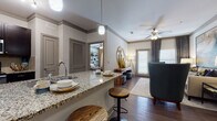 This 2-bedroom, 2-bathroom residence is designed with a modern aesthetic and functional layout across a single floor. The open-concept kitchen is a standout feature, outfitted with dark espresso cabinetry, granite countertops, a tile backsplash, and stainless steel appliances including a refrigerator, microwave, and range. A granite-topped breakfast bar with seating bridges the kitchen to the living area, making it ideal for both casual dining and entertaining. The living room offers a welcoming atmosphere with wood-style flooring, a ceiling fan, and natural light from large windows. Adjacent to it, the dining area provides an intimate setting. Both bedrooms are carpeted and include ceiling fans, natural light from windows, and closet space. The primary bedroom connects to a private bathroom featuring granite vanity countertops, dark cabinetry, and a bathtub with shower. The second bathroom mirrors the same refined finishes. Wood-style flooring flows through the main living areas, tying the space together with a cohesive, contemporary feel throughout.