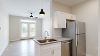This thoughtfully designed 530-square-foot, one-bedroom, one-bathroom apartment in Wilmington, NC offers an efficient and modern living experience. The open-concept kitchen and living area serves as the heart of the unit, featuring white shaker cabinets, a herringbone tile backsplash, stainless steel appliances including a refrigerator, dishwasher, microwave, and range, plus a kitchen island with an undermount sink and quartz-style countertops. A pendant light and ceiling fan complement the space, while French doors flood the living area with natural light and provide access to a private balcony with outdoor views. Light-toned luxury vinyl plank flooring flows seamlessly throughout the entire unit, enhancing the bright, airy ambiance created by neutral beige walls and white trim. The 140-square-foot bedroom includes a ceiling fan, a large window with natural light, and direct access to a dedicated closet with built-in shelving. The bathroom is finished with a white vanity, undermount sink, open corner shelving, and a louvered utility door. The overall design aesthetic is clean, contemporary, and move-in ready.
