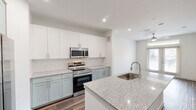 Located at 375 Greenbriar Rd in Fate, TX, this well-appointed one-bedroom, one-bathroom unit offers a thoughtfully designed single-floor layout with a clean, modern aesthetic throughout. The kitchen serves as the centerpiece of the living space and is outfitted with two-tone cabinetry — crisp white upper cabinets paired with soft sage-green lower cabinets — complemented by a classic white subway tile backsplash. A large granite-topped island with an undermount sink provides generous prep space and a natural gathering point. Stainless steel appliances include a French door refrigerator with ice dispenser, a slide-in electric range, an over-the-range microwave, and a dishwasher. An in-unit washer and dryer are also conveniently housed behind cabinetry nearby. Rich wood-look plank flooring runs throughout the entire unit, adding warmth and continuity. The bedroom is a comfortable, light-filled room with clean white walls and ample space. The bathroom features matching sage-green cabinetry with granite countertops, a white subway tile tub-shower combination, and direct access to a dedicated walk-in closet with built-in shelving and hanging rods. Recessed lighting and a ceiling fan contribute to a bright, airy ambiance throughout this move-in-ready home.