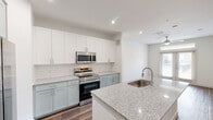 Located at 375 Greenbriar Rd in Fate, TX, this well-appointed one-bedroom, one-bathroom unit offers a thoughtfully designed single-floor layout with a clean, modern aesthetic throughout. The kitchen serves as the centerpiece of the living space and is outfitted with two-tone cabinetry — crisp white upper cabinets paired with soft sage-green lower cabinets — complemented by a classic white subway tile backsplash. A large granite-topped island with an undermount sink provides generous prep space and a natural gathering point. Stainless steel appliances include a French door refrigerator with ice dispenser, a slide-in electric range, an over-the-range microwave, and a dishwasher. An in-unit washer and dryer are also conveniently housed behind cabinetry nearby. Rich wood-look plank flooring runs throughout the entire unit, adding warmth and continuity. The bedroom is a comfortable, light-filled room with clean white walls and ample space. The bathroom features matching sage-green cabinetry with granite countertops, a white subway tile tub-shower combination, and direct access to a dedicated walk-in closet with built-in shelving and hanging rods. Recessed lighting and a ceiling fan contribute to a bright, airy ambiance throughout this move-in-ready home.