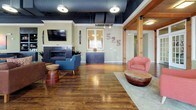 Located at 525 Kempsville Rd in Virginia Beach, VA, this single-floor amenity center blends industrial design with warm, welcoming interiors. The spacious lounge area serves as the heart of the space, featuring rich hardwood floors, exposed structural timber columns, a sleek fireplace, a wall-mounted TV, and an open, dark-painted ceiling that adds an industrial edge. Large multi-pane windows flood the space with natural light, while seating nooks and a built-in counter bar provide comfortable gathering spots.

The game room is generously proportioned, accommodating multiple billiard tables beneath pendant lighting, with continued hardwood flooring and expansive windows along one wall offering abundant daylight.

The fully equipped kitchen features dark cabinetry, granite countertops, stainless steel appliances including a full-size refrigerator and dishwasher, and a bright window backsplash area — ideal for resident events and gatherings.

The fitness area includes dedicated cardio equipment from Matrix, wall-mounted TVs, and rubber-topped flooring for comfort and safety. Adjacent to this, a yoga and movement studio showcases light hardwood floors, exposed brick accent walls, full-wall mirrors, and exercise equipment including stability balls — an inspiring setting for group classes or individual practice. French doors connect the studio seamlessly to the rest of the facility.