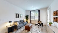 Located at 2551 Frontier Dr in Pittsburgh, PA, this well-appointed one-bedroom, one-bathroom residence offers a thoughtfully designed single-floor layout with a clean, contemporary aesthetic throughout. The open-concept kitchen and living area serves as the heart of the home, featuring light wood-style flooring, crisp white walls, and abundant natural light from large windows with outdoor views. The kitchen is outfitted with white shaker cabinetry, stainless steel appliances including a refrigerator, range, and microwave, a white subway tile backsplash, and a center island with a quartz-style countertop, an undermount sink with a matte black faucet, and seating — all illuminated by a striking pendant light. The living area is bright and welcoming, with large windows framing outdoor greenery and ample room for comfortable furnishings. The bedroom offers plush carpeting, a generous double-door closet with dark-painted doors, and a large window that fills the space with natural light. The bathroom features wood-style flooring, a white vanity, and a full tub-shower combination with classic white subway tile. Dark-painted interior doors add a modern contrast throughout the residence, creating a cohesive and stylish design from room to room.