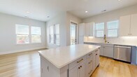 Located at 4312 Yancey Rd in Charlotte, NC, this well-appointed 2-bedroom, 2-bathroom home offers a clean, modern aesthetic with thoughtfully designed living spaces across a single floor. Light hardwood flooring flows throughout, complementing the bright, neutral palette that defines the interior.

The open-concept kitchen and living area serves as the heart of the home. The kitchen is outfitted with two-tone cabinetry — white upper cabinets and slate-blue lower cabinets — topped with crisp white quartz countertops and a herringbone tile backsplash. A large central island provides additional prep and seating space, while stainless steel appliances, including a refrigerator, range, microwave, and dishwasher, complete the setup. A gold-toned faucet adds a refined accent. Abundant windows fill the living area with natural light.

A clean hallway connects the bedrooms and bathrooms. Both bedrooms are generously sized, each featuring multiple windows with outdoor views, ceiling fans, and ample natural light. The primary bedroom leads to an en-suite bathroom with a double-sink vanity featuring blue-gray cabinetry, a glass-enclosed walk-in shower with white subway tile, and an adjacent walk-in closet with built-in shelving and hanging rods. The layout is efficient, comfortable, and move-in ready.