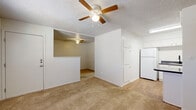 This single-floor unit offers a practical and efficiently designed layout across five distinct areas. The open living space is finished with warm beige carpeting and features a textured popcorn ceiling with a ceiling fan and light fixture, lending a casual, comfortable atmosphere throughout. A half-wall partition subtly separates the living area from the kitchen, which is outfitted with white cabinetry, dark granite-style countertops, a double-basin sink, a white refrigerator, and an electric cooktop. The kitchen also includes a peninsula that serves as a breakfast bar, with durable wood-look flooring completing the space. The bedroom area is carpeted and benefits from a window fitted with horizontal blinds, allowing natural light to filter in, along with a wall-mounted air conditioning unit for climate control. The bathroom is clean and straightforward, featuring a full-size soaking tub with a tiled surround and a showerhead, alongside a toilet and wood-look flooring. A dedicated utility closet houses a water heater and electrical panel, with built-in shelving on both sides offering additional storage. Overall, the space presents a functional and well-organized layout suited to efficient everyday living.