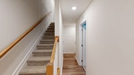 This three-story home offers four bedrooms and three bathrooms, thoughtfully distributed across its floors to maximize functionality and comfort. The ground level houses an attached single-car garage with an automatic door opener, providing convenient and secure parking alongside additional utility space.

The main living floor serves as the heart of the home, centered around a bright, open-concept kitchen and living area. The kitchen is outfitted with white shaker-style cabinetry, granite countertops, stainless steel appliances, a tiled backsplash, and a central island with a built-in sink and pendant lighting overhead. Light hardwood flooring runs throughout this level, complementing the clean, neutral color palette. A sliding glass door provides access to an outdoor area, allowing natural light to pour into the living space.

The upper floor accommodates the bedrooms, including a generously sized primary bedroom. Soft carpeting lines the bedroom floors, while the hallways continue the hardwood theme. Two staircases with warm wood railings connect the floors, enhancing the home's vertical flow. The bathrooms are finished with granite-topped vanities, undermount sinks, chrome fixtures, and tile flooring, with at least one full bath featuring a tub-shower combination. Throughout, the home maintains a consistent, modern aesthetic with neutral tones and quality finishes.