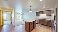 Located at 19948 Headwaters Blvd N in Forest Lake, Minnesota, this single-floor, one-bedroom, one-bathroom unit offers a well-organized and functional layout. The open-concept kitchen and living area forms the heart of the home, featuring rich dark-stained cabinetry, granite-look countertops, a central island with additional storage, and a full suite of stainless steel appliances including a refrigerator, range, microwave, and dishwasher. Light hardwood-style flooring runs throughout the kitchen and living space, while a stylish pendant chandelier adds a warm, inviting ambiance. The living area extends toward a sliding glass door that opens to a balcony, allowing for natural light and outdoor views, and is complemented by a ceiling fan overhead. The bedroom is a comfortable, carpeted retreat with a large window that fills the room with natural light and offers views of the surrounding area. The full bathroom is finished with wood-tone cabinetry, a framed mirror, white countertop, and a combination tub and shower. A dedicated laundry room houses a full-size washer and dryer along with a wire shelving unit for added storage. The unit also includes a separate closet, providing ample storage throughout.