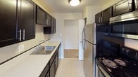This one-bedroom, one-bathroom unit offers a thoughtfully designed single-floor layout that balances function and comfort. The kitchen is a standout feature, showcasing upgraded espresso cabinetry with sleek hardware, light countertops, a stainless steel sink, and a full suite of stainless steel appliances including a refrigerator and range. Light-toned vinyl flooring runs throughout the kitchen, creating a clean, practical workspace.

The living area flows openly from the kitchen, with neutral-toned carpet underfoot and soft, muted wall colors that create a calm atmosphere. A ceiling fan provides additional comfort, while multiple windows along the perimeter flood the space with natural light and offer views of surrounding greenery. Baseboard heating units run along the walls, providing efficient warmth throughout.

The bedroom is generously proportioned with plush carpeting, a window with natural views, and a baseboard heater. A closet provides convenient storage. The bathroom features light vinyl flooring, a tiled shower/tub combination, a window for natural ventilation, a vanity with ample counter space, and a baseboard heater, completing this well-appointed unit.