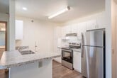 This efficiently designed 3-bedroom, 1-bathroom single-story unit offers a thoughtfully arranged floor plan that maximizes its compact footprint. The open-concept living and kitchen area serves as the heart of the space, featuring vaulted ceilings that create a heightened sense of openness. A peninsula with granite-look countertops defines the kitchen zone, which is equipped with stainless steel appliances including a refrigerator, electric range, and dishwasher, complemented by ample white cabinetry. A sliding glass door in the living area provides natural light and outdoor access.

Wood-look laminate flooring runs consistently throughout the unit, lending a cohesive, modern appearance. The primary bedroom includes a ceiling fan, a closet with sliding wood-panel doors, and natural light. A second bedroom also features a ceiling fan and two windows with outdoor views. A third bedroom offers wire shelving for additional storage. The shared full bathroom includes a single-sink vanity with white cabinetry, a toilet, and a tub-shower combination, all finished in a clean, neutral palette.