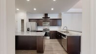 Located at 5223 Hunters Ridge Dr in New Port Richey, Florida, this single-story home offers a thoughtfully designed layout with consistent, modern finishes throughout. The kitchen is a standout feature, showcasing rich dark espresso cabinetry, granite countertops, a central island, a wall-mounted range hood, and a full suite of stainless steel appliances. Light wood-look flooring runs through the main living areas, complementing the neutral wall tones and crown molding that are present throughout the home.

The dining area is defined by an elegant tray ceiling with crown molding detail and a classic chandelier, lending a refined character to the space. An adjacent living area opens seamlessly from the kitchen via a granite-topped breakfast bar, creating a cohesive, open-concept feel. Bedrooms feature plantation shutters and walk-in closets, adding both functionality and charm.

The bathroom includes tile flooring, a granite-topped dark vanity, and a full tub-shower combination with floor-to-ceiling tile surround and brushed nickel fixtures. A dedicated laundry area with tile flooring provides added convenience. The attached garage features an epoxy-coated floor, an automatic opener, and interior access, completing this well-finished home.