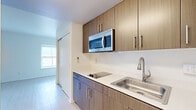 Located at 302 Arizona Ave in the heart of Santa Monica, CA, this one-bedroom, one-bathroom unit offers a thoughtfully designed layout that maximizes every square foot of its compact footprint. Light wood-style flooring runs throughout the living areas, lending a clean, contemporary aesthetic complemented by bright white walls and natural light from well-placed windows.

The kitchen features warm wood-toned cabinetry with sleek bar-pull hardware, white countertops, a stainless steel single-basin sink, an electric cooktop, and an over-the-range stainless steel microwave. Upper and lower cabinets provide ample storage, while the streamlined design keeps the space feeling open and efficient. A sliding door from the main living area offers convenient access between rooms.

The bedroom is a generously proportioned space relative to the overall unit, accommodating comfortable furnishing arrangements. A window allows natural light to fill the room, enhanced by the light-toned flooring and neutral wall palette.

The bathroom is outfitted with a full soaking tub and shower combination, accented by a distinctive teal tile border against white subway tiles. A wall-mounted sink and large mirror round out the clean, functional design. A wall-mounted air conditioning unit serves the living area, ensuring year-round comfort in this well-located Santa Monica residence.