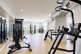 Located at 4111 N Drinkwater Blvd in Scottsdale, Arizona, this well-appointed fitness center offers a generously sized, single-floor layout designed to accommodate a comprehensive range of workout needs. The facility is bathed in natural light, courtesy of large floor-to-ceiling windows along one side of the space, providing bright, open views of the surrounding Scottsdale environment. Light hardwood-style flooring runs throughout, lending a clean and modern aesthetic that complements the crisp white walls and exposed industrial-style ventilation ductwork overhead.

The cardio zone features treadmills, elliptical machines, a stair climber, and a stationary bike, all positioned to take advantage of the abundant natural light streaming in from the expansive window wall. A dedicated strength training area houses a variety of cable and weight machines, with a separate section offering free weights and a dumbbell rack. An open stretch and movement area is anchored by a motivational neon "Don't Quit" wall display and a wall-mounted ballet barre, ideal for stretching or barre-style workouts. A vibrant Arizona-themed mural adds a colorful, local character to the space. Recessed lighting supplements natural light throughout, and the facility is accessed via glass-panel double doors, contributing to its clean, professional atmosphere.