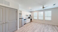 Located at 555 Linger Longer Dr on Johns Island, SC, this single-floor unit offers a clean, modern layout with thoughtful design details throughout. Light wood-look flooring runs continuously across all areas, lending a cohesive and airy feel to the space. The open living area is bright and welcoming, with multiple windows fitted with white blinds that allow generous natural light to fill the room. Ceiling fans are present throughout, contributing to both comfort and airflow.

The kitchen is a standout feature, outfitted with white shaker-style cabinetry, a subway tile backsplash, granite countertops, and a full suite of stainless steel appliances including a refrigerator, dishwasher, electric range, and over-the-range microwave. An open wine rack adds a charming accent to the upper cabinetry.

The hallway provides functional connectivity between the main living area and the secondary spaces, with gray-paneled doors adding a subtle contrast to the neutral white walls. The bathroom is clean and efficient, featuring a tub-shower combo with built-in shelving, a white vanity with granite countertop, and matching wood-look flooring. The overall palette of whites, grays, and natural wood tones creates a calm, modern atmosphere throughout.