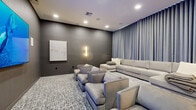 Located at 72 Eagle Rock Ave in East Hanover, NJ, this sophisticated screening room delivers a premium home theater experience within a well-appointed, single-level living space. The room is designed with a distinctly cinematic aesthetic, characterized by deep charcoal-gray walls that create an immersive, low-distraction environment ideal for viewing.

A large wall-mounted flat-screen television serves as the focal point, flanked by flush-mounted in-wall speakers that form a dedicated surround sound system. Recessed ceiling lighting and elegant vertical wall sconces provide warm, dimmable illumination that complements the room's moody ambiance.

Seating is generous and thoughtfully arranged, combining a large sectional sofa upholstered in light neutral fabric with a row of plush, matching lounge chairs positioned for optimal screen viewing. A patterned area rug anchors the seating area, adding textural contrast to the space.

Floor-to-ceiling blue-gray drapery spans an entire wall, lending a dramatic, theatrical quality to the room and enhancing its acoustic properties. A popcorn machine stationed near the rear entry adds a fun, functional touch that reinforces the space's entertainment-focused purpose.

Overall, this screening room blends modern design with comfort-forward furnishings, making it an inviting and fully equipped venue for movies, sports, and shared viewing experiences.