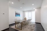 Located at 1424 Highland Rd W in Kitchener, Ontario, this single-room meeting or gathering space offers a clean, contemporary design well-suited for small group meetings, collaborative sessions, or social gatherings. The room is finished with crisp white walls and recessed pot lighting that evenly illuminates the space, creating a bright and inviting atmosphere. Large-format dark grey tile flooring runs throughout, grounding the room with a sleek, modern aesthetic, while a neutral area rug beneath the central table adds warmth and texture. The centerpiece of the room is a long, light wood-toned rectangular table surrounded by stylish gold wire chairs, comfortably seating up to ten occupants. A vibrant cityscape canvas print mounted on the wall introduces a bold pop of colour and serves as the room's primary decorative accent. Sheer white curtains frame a window along one wall, softening the natural light and contributing to the room's airy feel. Climate control is managed via a wall-mounted thermostat, and ventilation grilles are integrated into the ceiling and walls. A solid commercial-grade entry door with an automatic closer ensures easy and secure access. The overall ambiance is modern, functional, and thoughtfully curated.