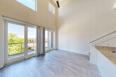 Located at 2115 Piedmont Rd NE in Atlanta, GA, this two-story residence offers a thoughtfully designed layout spread across two distinct floors. The main level is the architectural centerpiece, showcasing dramatic double-height ceilings that flood the open living area with natural light through tall clerestory windows and full-height glass French doors. These doors open to a private balcony, extending the living space outdoors with views of surrounding greenery. Light-toned hardwood-style flooring runs throughout the main level, complementing the clean, neutral palette. The kitchen features a granite-topped peninsula, dark cabinetry, stainless steel appliances including a range and microwave, and pendant lighting that descends dramatically from the soaring ceiling above. A carpeted staircase with a metal grid railing leads to the upper level, where the bedroom is tucked away for privacy. The upper floor is finished with plush carpet and features an elegant chandelier, adding a refined touch. The full bathroom is well-appointed with dark wood vanity cabinetry, a quartz countertop, and a shower/tub combination. Hallways on both floors connect each space efficiently, with stylish pendant lighting accenting the lower corridor. This residence combines modern industrial design elements with warm finishes throughout.