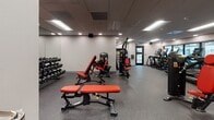 Located at 414 N Fifth Ave in Tucson, Arizona, this modern fitness center is designed to support a comprehensive range of workout routines within a single, well-organized floor. The space is finished with durable rubber flooring throughout, providing both traction and impact absorption for users across all activity zones.

The cardio area is lined with a row of treadmills and elliptical machines equipped with digital screens, positioned alongside large glass windows that bring in natural light and offer views into adjacent areas, creating an open and energizing atmosphere. A drop ceiling with recessed and panel lighting ensures consistent, bright illumination across the entire facility.

The strength training zone features a robust selection of Hoist cable machines and Matrix weight benches with red upholstery, complemented by a full rack of dumbbells along the mirrored wall — catering to both machine-based and free weight training. A standout architectural feature is the built-in climbing wall, adding a unique functional fitness element to the space.

A water fountain is conveniently installed near the entry corridor, which also provides glass-door access to adjacent building spaces. The facility maintains a clean, professional aesthetic with neutral gray and white walls, a drop-panel ceiling, and a practical, clutter-free layout designed to maximize usability and flow for all fitness levels.