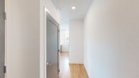 Located at 6609 E Warren Dr. in Denver, CO, this thoughtfully designed one-bedroom, one-bathroom unit offers a clean, modern aesthetic throughout its well-utilized single-floor layout. The open-concept kitchen and living area serves as the heart of the home, featuring light hardwood-style flooring, sleek gray cabinetry with brushed metal hardware, and a tall vertical window that draws in natural light and frames outdoor views. A private entry door with a glass panel further brightens the living space, complemented by recessed lighting overhead. The hallway connecting the main living area to the private quarters is clean and minimal, with a contemporary gray door and recessed ceiling fixtures adding a polished touch. The generously sized bedroom is carpeted for comfort and boasts a large bank of windows with views of the surrounding Denver neighborhood, plus a ceiling fan for year-round climate control. A dedicated walk-in closet off the bedroom provides ample storage with multi-tiered wire shelving and hanging rods. The full bathroom features a tiled tub-shower combo with a curved curtain rod, a white vanity with a light countertop, and warm hardwood-style flooring, completing this well-appointed and move-in-ready Denver residence.