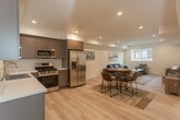 Located at 7053 Jordan Ave in the Canoga Park neighborhood of Los Angeles, this single-floor unit offers a thoughtfully designed, modern living space with an open-concept layout that seamlessly connects the kitchen, dining, and living areas. Light-toned hardwood-style flooring runs throughout, complementing the crisp white walls and recessed lighting that create a bright, welcoming atmosphere.

The kitchen is well-appointed with sleek gray flat-front cabinetry, white quartz countertops, and a full suite of stainless steel appliances, including a gas range, microwave, dishwasher, and a side-by-side refrigerator with an ice and water dispenser. A window above the sink allows natural light to fill the space. Ample upper and lower cabinet storage adds to the kitchen's practicality.

The open dining area flows naturally into the living room, which features a large window that brings in additional natural light. The living area offers generous space for relaxing or entertaining, with defined zones for seating and media.

The bathroom is finished with the same contemporary aesthetic, featuring light wood-look flooring, a gray vanity with a white countertop, a glass-enclosed shower and tub combination, and clean white walls throughout. The overall design is modern, functional, and move-in ready.