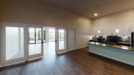 This well-designed single-floor unit offers a contemporary open-concept layout with impressive architectural details throughout. The expansive living area is anchored by soaring ceilings and dramatic floor-to-ceiling windows and sliding glass doors that flood the space with natural light and provide direct access to a private balcony with outdoor views. Rich, dark hardwood-style flooring runs throughout the main living areas, adding warmth and continuity.

The kitchen is thoughtfully appointed with white upper cabinetry, dark lower cabinetry, a dark tile backsplash, quartz countertops, stainless steel appliances, a peninsula island with an undermount sink featuring a matte black faucet, and pendant lighting above. A stylish sliding barn door leads to a hallway connecting the remaining areas of the unit.

An in-unit laundry area is conveniently accessible from the main living space. The bedrooms are carpeted and well-proportioned, each equipped with ceiling fans and generous closet space, including a walk-in closet with built-in shelving and hanging rods. The bathroom features a dual-sink vanity with dark wood cabinetry, a framed mirror with matte black hardware, and a tiled soaking tub and shower combination. The overall aesthetic is clean, modern, and move-in ready.