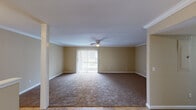 This single-floor residence offers a thoughtfully laid-out interior with a warm, neutral color palette carried consistently throughout. The living room is generously sized, featuring plush wall-to-wall carpeting, crown molding, and a ceiling fan with integrated lighting. A sliding glass door floods the space with natural light and provides direct access to an outdoor area, complemented by vertical blinds for privacy and light control. Adjacent to the living room, the dining area transitions seamlessly via warm-toned tile flooring, accented by elegant crown molding and a flush-mount ceiling light. An open pass-through connects directly to the kitchen, which is equipped with rich wood cabinetry, dark granite countertops, a stainless steel double-basin sink, a dishwasher, and an electric range — all anchored by a window that invites natural light. The bedrooms are carpeted and comfortably proportioned, each featuring windows with blinds that provide views of the surrounding exterior. The layout, as visible in the dollhouse view, is compact yet efficiently organized, offering clear spatial flow between the living, dining, kitchen, and sleeping areas. The overall ambiance is clean, functional, and move-in ready.