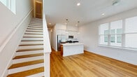 Located on Oconee Street in Athens, Georgia, this contemporary two-story home offers four bedrooms and five bathrooms across a well-organized layout. The main floor hosts the larger share of the living space, featuring an open-concept kitchen and living area bathed in natural light from large windows. The kitchen is a standout, boasting a spacious white island with an integrated sink, stainless steel appliances including a refrigerator, range, and microwave, white shaker-style cabinetry, dark countertops, and stylish pendant lighting. The living area connects seamlessly, with a staircase and transom window adding vertical interest. Warm hardwood-style flooring flows consistently throughout both levels, complementing the clean white walls and modern black hardware details. Bedrooms are bright and well-proportioned, several featuring ceiling fans, large windows with exterior views, and access to dedicated closets. One bedroom conveniently connects to a stacked washer and dryer laundry area. The five bathrooms include a pedestal-sink powder room and full bathrooms with subway-tiled tub-shower combinations. The upper floor provides additional bedroom accommodations with their own closets and bathrooms, offering privacy and flexibility. The overall aesthetic is clean, modern, and move-in ready.
