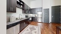 Located at 1505 Fifth Ave N in Nashville's Germantown neighborhood, this single-floor residence showcases a thoughtfully designed interior with striking architectural details. Soaring ceilings create an impressive sense of volume throughout the living spaces, while large windows fitted with horizontal blinds invite abundant natural light and views of surrounding greenery.

The living area is highlighted by its generous height, with crisp white walls providing a gallery-like backdrop for large-scale artwork. Warm hardwood flooring anchors the space, complemented by a colorful area rug and natural-material accents that add texture and visual interest.

The kitchen is well-equipped and features dark espresso cabinetry paired with granite countertops, a classic white subway tile backsplash, and a full suite of stainless steel appliances. Tall upper cabinets take advantage of the elevated ceilings, maximizing storage throughout.

The bedrooms maintain the home's bright, airy aesthetic with neutral tones, plush carpeting, and oversized windows that frame outdoor views. The bathroom is finished with large-format tile flooring, a dark vanity with granite countertop, vessel sink, and a five-panel charcoal door that adds a bold, modern accent. Overall, the space conveys a cohesive contemporary style with warm, inviting finishes.