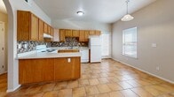 Located at 9010 Betel Dr in El Paso, Texas, this single-story, 2-bedroom, 1-bathroom home offers a practical and well-organized layout. The combined kitchen and dining area serves as the heart of the home, featuring warm honey-toned wood cabinetry, a mosaic tile backsplash, white appliances including an electric range, dishwasher, and refrigerator, and a convenient peninsula with additional workspace. Large terracotta-style floor tiles extend throughout the kitchen and dining area, complemented by a pendant light and a window that fills the space with natural light. An elegant arched doorway connects the kitchen to the living room, which is outfitted with a ceiling fan. Both bedrooms are carpeted and finished with neutral tones, offering a calm and comfortable atmosphere. Each room includes a window with blinds for natural light and privacy. The primary bedroom features access to a walk-in closet with built-in shelving, providing ample storage. The bathroom includes a single-sink vanity with wood cabinetry, a large mirror, tile flooring, and a full tub-shower combo with tiled surround. A hallway connects the main living areas to the bedrooms, and the home also includes an outdoor patio space.