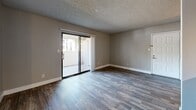 Located at 1975 E University Dr in Tempe, Arizona, this one-bedroom, one-bathroom apartment offers a well-designed layout with modern finishes throughout. The open-concept living room and kitchen area is anchored by rich, dark wood-style plank flooring and neutral gray walls, creating a clean and contemporary aesthetic. A textured ceiling and ceiling fan add character, while sliding glass doors flood the space with natural light and provide direct access to a private outdoor patio. The kitchen is well-appointed with gray shaker-style cabinetry, light quartz countertops, a white subway tile backsplash, and a full suite of stainless steel appliances, including a range, over-the-range microwave, and refrigerator. The bedroom offers plush carpeting, a ceiling fan with light fixture, and a window with vertical blinds that brings in additional natural light. A dedicated closet provides convenient storage. The bathroom features wood-style flooring, a white vanity with quartz countertop, and a tub-shower combination with large-format gray tile surround. The overall ambiance is fresh, cohesive, and move-in ready, with consistent neutral tones tying each space together seamlessly.