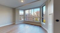Located at 1201 N Sandburg Terr in Chicago's sought-after Gold Coast neighborhood, this single-floor residence combines contemporary design with functional living. The space is defined by expansive floor-to-ceiling windows that wrap around the main living area, flooding the interior with abundant natural light and framing dynamic views of the surrounding Chicago cityscape, including neighboring brick buildings and high-rise towers on the horizon.

Light-toned hardwood flooring runs throughout the living areas, contributing to a bright, airy atmosphere. The kitchen is outfitted with sleek, modern cabinetry in a two-tone palette of slate blue upper cabinets and light wood lower cabinets, complemented by crisp white quartz countertops, a textured tile backsplash, open floating shelves, and stainless steel appliances including a built-in oven and induction cooktop.

The bedroom features mirrored sliding closet doors that enhance the sense of space, alongside the same warm hardwood flooring found throughout. The bathroom is finished with large-format white tile flooring, a wood-toned vanity with white countertop, and a recessed-light ceiling, offering a clean and contemporary aesthetic. Recessed lighting and neutral warm-gray walls complete the polished, modern feel of this well-appointed Chicago residence.