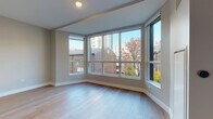 Located at 1201 N Sandburg Terr in Chicago's sought-after Gold Coast neighborhood, this single-floor residence combines contemporary design with functional living. The space is defined by expansive floor-to-ceiling windows that wrap around the main living area, flooding the interior with abundant natural light and framing dynamic views of the surrounding Chicago cityscape, including neighboring brick buildings and high-rise towers on the horizon.

Light-toned hardwood flooring runs throughout the living areas, contributing to a bright, airy atmosphere. The kitchen is outfitted with sleek, modern cabinetry in a two-tone palette of slate blue upper cabinets and light wood lower cabinets, complemented by crisp white quartz countertops, a textured tile backsplash, open floating shelves, and stainless steel appliances including a built-in oven and induction cooktop.

The bedroom features mirrored sliding closet doors that enhance the sense of space, alongside the same warm hardwood flooring found throughout. The bathroom is finished with large-format white tile flooring, a wood-toned vanity with white countertop, and a recessed-light ceiling, offering a clean and contemporary aesthetic. Recessed lighting and neutral warm-gray walls complete the polished, modern feel of this well-appointed Chicago residence.
