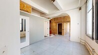 Located at 725 S Spring St in Downtown Los Angeles, this one-bedroom, one-bathroom unit offers a generously proportioned floor plan with a distinctly eclectic character. The main living and kitchen area is the heart of the space, showcasing a bold multicolored checkered tile floor that anchors the room's artistic aesthetic. A striking mustard-yellow accent wall frames the kitchen, which features white lower cabinetry, a countertop sink, and standard appliances. An open shelving unit and dark wood upper cabinets add functional storage alongside visual interest. Overhead, an eye-catching branching light fixture with globe bulbs provides ambient illumination alongside recessed track lighting.

An adjacent living area features a full wall clad in warm horizontal wood planks, complemented by a ceiling fan and an ornate pendant light, creating a cozy, textured contrast to the open kitchen zone. The bedroom is accessed via a hallway and features large black-framed windows that bring in natural light, with OSB-paneled walls lending a raw, industrial character. A classical arched doorway connects rooms, nodding to the building's historic bones. The bathroom includes a tub-shower combo with frosted glass doors, a vanity with granite countertop, and tile flooring. A utility room and additional hallway complete the layout.