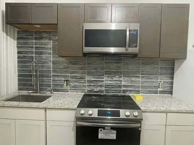 Modern kitchen with stainless steel appliances, quartz countertops, island and marble flooring - 31 Clinton Ave