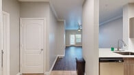 Located in Orlando, FL, this 1-bedroom unit offers a thoughtfully designed single-floor layout that maximizes functionality and comfort. The open-concept living room is finished with warm, wood-style plank flooring and neutral gray tones throughout, creating a clean and inviting atmosphere. Crown molding adds a refined architectural detail, while a ceiling fan with a light fixture provides both style and practicality. Natural light filters in through double windows fitted with blinds, and a glass-paneled door leads to a private outdoor area overlooking lush tropical greenery — a serene Florida backdrop. The kitchen is designed for efficiency, featuring a galley-style layout with light tile flooring, contemporary wood-tone cabinetry, and crisp white countertops. Stainless steel appliances — including a refrigerator, range, microwave, and dishwasher — add a modern touch. A pass-through counter with an integrated sink connects the kitchen to the living space, enhancing the open feel. The bedroom is accessible via a wide doorway from the living area and continues the same wood-style flooring and neutral palette. This unit presents a cohesive, move-in-ready interior with clean finishes throughout.