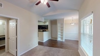 This single-story, one-bedroom, one-bathroom residence offers a thoughtfully designed layout that balances functionality and comfort. The living area is defined by vaulted ceilings and ceiling fans, creating an airy, open atmosphere. Plush carpeting covers the main living and bedroom spaces, while durable hardwood-style flooring runs through the entryway and kitchen, providing a clean visual contrast. Large windows allow natural light to fill the living area, offering pleasant outdoor views.

A built-in shelving unit adds a distinctive architectural detail to the living space, providing display and storage options. The adjacent dining area features a pendant light fixture and additional windows, enhancing the bright, welcoming feel of the shared living space.

The kitchen is well-equipped with dark espresso cabinetry, matching black appliances including a range, microwave, and refrigerator, complemented by a double-basin sink and tile flooring. A breakfast bar connects the kitchen to the main living area.

The bedroom is generously sized with plush carpet, a ceiling fan, a walk-in closet, and an additional closet for ample storage. A built-in desk with shelving offers a practical workspace. The bathroom includes a full tub-shower combination with tile surround. A dedicated utility closet houses the water heater with washer/dryer hookups conveniently nearby.