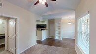 This single-story, one-bedroom, one-bathroom residence offers a thoughtfully designed layout that balances functionality and comfort. The living area is defined by vaulted ceilings and ceiling fans, creating an airy, open atmosphere. Plush carpeting covers the main living and bedroom spaces, while durable hardwood-style flooring runs through the entryway and kitchen, providing a clean visual contrast. Large windows allow natural light to fill the living area, offering pleasant outdoor views.

A built-in shelving unit adds a distinctive architectural detail to the living space, providing display and storage options. The adjacent dining area features a pendant light fixture and additional windows, enhancing the bright, welcoming feel of the shared living space.

The kitchen is well-equipped with dark espresso cabinetry, matching black appliances including a range, microwave, and refrigerator, complemented by a double-basin sink and tile flooring. A breakfast bar connects the kitchen to the main living area.

The bedroom is generously sized with plush carpet, a ceiling fan, a walk-in closet, and an additional closet for ample storage. A built-in desk with shelving offers a practical workspace. The bathroom includes a full tub-shower combination with tile surround. A dedicated utility closet houses the water heater with washer/dryer hookups conveniently nearby.