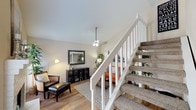 This two-story home offers a well-organized layout designed for comfortable everyday living. The main level features a living area with warm hardwood flooring, a ceiling fan, and vaulted ceilings that lend an open, airy feel. A white-railed staircase with carpeted treads connects the two floors, serving as a functional architectural centerpiece. Adjacent to the living area is a dedicated dining space equipped with a pendant light fixture and hardwood floors, providing an intimate setting for meals. The galley-style kitchen features dark cabinetry, granite-style countertops, a stainless steel sink, and black appliances, offering ample storage and counter space. A closeted laundry area with a top-loading washer is conveniently tucked within the home. Upstairs, carpeted bedrooms provide comfortable retreats, each with ceiling fans and windows that invite natural light. A walk-in closet is accessible from one of the bedrooms. The bathrooms include a tub-shower combination with white tile surround and a vanity with a granite-style countertop and mirror. Throughout the home, neutral wall tones create a cohesive and welcoming ambiance.