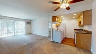 Located at 6757 Highland Greens Dr in West Chester, Ohio, this single-floor unit offers a straightforward and functional layout well-suited for everyday living. The open-concept living area is generously sized, finished with wall-to-wall carpeting and equipped with a ceiling fan and a wall-mounted air conditioning unit. Vertical blinds frame the sliding door, allowing natural light to flow into the space. The kitchen is positioned adjacent to the living area and features warm-toned wood cabinetry, dark granite-style countertops, a stainless steel sink, and hardwood flooring. White appliances include a refrigerator, electric range, and washer, all neatly arranged within the compact kitchen footprint. Recessed lighting overhead adds a clean, finished look to the kitchen area. The bedroom is a comfortable, carpeted room with a window offering views of the surrounding greenery, complemented by a wall-mounted AC unit and baseboard heating for year-round climate control. The full bathroom includes a tub-shower combination, a window for natural ventilation, tile flooring, and classic white fixtures. Baseboard heating is present throughout the unit, ensuring consistent warmth. The overall ambiance is clean, neutral, and move-in ready.