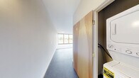 Located at 131 E Green St, Unit 316 in Ithaca, NY, this one-bedroom, one-bathroom unit offers a modern, industrial-influenced design across a single floor. The open-concept living and kitchen area features a speckled dark floor, white cabinetry with dark countertops, and white appliances including a stove and refrigerator. Exposed cylindrical ductwork runs along the ceiling, lending an urban, loft-like character to the space. Pendant lighting above the kitchen adds functional brightness to the area.

The spacious bedroom is carpeted and bathed in natural light through large wood-framed windows that frame views of both the surrounding cityscape and lush green hillside, offering a pleasant contrast of urban and natural scenery. A second set of floor-to-ceiling wood-framed windows in the living area further enhances the connection to the outdoors and fills the unit with abundant daylight.

The bathroom is finished with dark slate-style tile flooring and includes a walk-in shower with a chrome showerhead, a wall-mounted vanity, and clean white walls that create a crisp, minimalist aesthetic. A closet provides dedicated storage. The unit's neutral color palette of whites and grays throughout creates a cohesive, contemporary feel well-suited for comfortable everyday living.